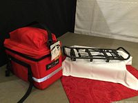 Red deluxe expandable bike rack pack with reflective stripe and black metal bike rack on white fabric background.