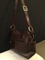 Side view of dark brown leather LaDiva shoulder bag showing adjustable strap with brass buckle and brass connecting rings, and side pocket