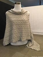 Full view of the cashmere poncho displayed on a mannequin showcasing its shape and cable knit design.