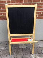 Front view showing black chalkboard surface with wooden frame and red chalk tray containing chalk sticks.