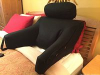 Front angle view showing the black cushioned bed lounge with armrests and rounded padded headrest on wooden bed frame.