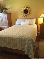 Photo of the queen bed made with the grey and white bedspread showing full bedding set including shams and decorative pillow on wooden bed frame in bedroom.