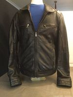 Front view of black leather jacket on mannequin showing zipper, chest and side pockets, and collar detail.