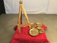 Wooden Florentine style plate stand shown upright with four matching round coasters laid next to it on a red cloth.