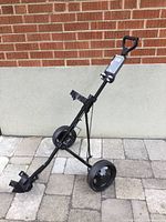 Photo of fully assembled folding golf push cart, showing 2 large wheels, black metal frame, handle, and accessory holder attachment.