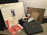 Wide shot of whiteboard, corkboard, file folders, packs of lined paper, jar of office supplies, Post-it notes, and miscellaneous desktop supplies.