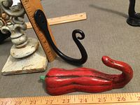 Close-up of black S-hook and red ceramic chili pepper hook next to ruler for size reference