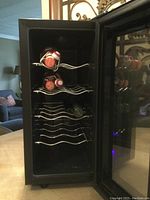 Open door view of the wine cooler showing interior with 4 curved metal racks holding wine bottles horizontally.