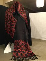 Full view of scarf draped over mannequin, showing red pattern on black and fringed ends