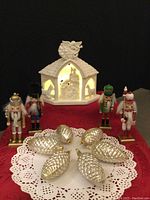 Full set showing porcelain manger lit with mini lights, four nutcracker soldiers in different colors, and six glass pine cone ornaments on doily.