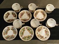 Top view of six tea cups and six saucers arranged on black surface showing colorful scenic designs and gold accents.