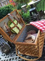 Wicker picnic basket open showing wine glasses, plates, and checkered cloth napkin inside.