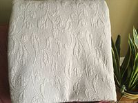 Taupe colored quilted bedspread folded, showing textured leaf pattern on surface.