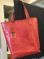 Front angle of red leather tote bag with alligator embossing, showing shoulder straps and logo tag