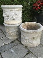 Three stacked cement planters showing the raised floral design and weathered cement surface on outdoor stone patio