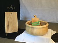 Photo showing the wooden cutting board and the large wooden bowl with cabbage shredder inside it, displayed on a white cloth.