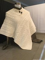 Front side view of cream cable knit wool poncho on mannequin showing button collar and knit patterns.