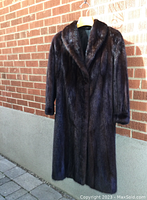 Full front view of a dark brown full length mink coat hanging against a brick wall outdoors in natural light.