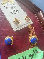 Photo showing two sets of stud earrings on a paper card, one with white stones and the other with blue stones, marked 14k gold