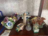 Photo of the lot including two bone china flower sculptures and several animal-shaped salt and pepper shakers, a small cart figurine, and a winged angel figurine.