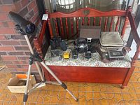 Photo showing full lot including Bushnell telescope on tripod, two pairs of binoculars, multiple cameras and accessories on bench.
