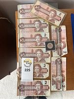 Photo of nine Canadian 2 dollar bills and one Canadian Toonie coin laid out on a table.