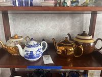 Overview of three ceramic teapots and one copper teapot on a shelf