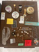 Overall collection of costume jewelry displayed on wood table including rings, earrings, chains, pins, and watch.
