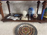 Wide view of all items on and in front of a wooden table, showing crystal vase, porcelain vases, LLADRO cherub, Mexican metal plate, and other items.