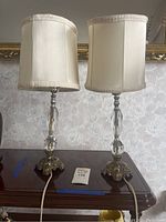 Front view of two matching ornate vintage nightstand lamps showing fabric shades and clear faceted glass sections on metal bases with detailed antique-style designs.