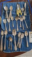 Set of silver plated flatware including spoons, knives and forks laid out on cloth.