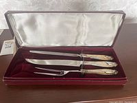 Three-piece sterling silver handled carving set displayed in a fitted box with white satin lid lining and red velvet interior.
