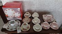 Photo of assorted teacups, saucers, and boxed Christmas dinner set on table.
