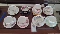 Seven teacups and saucers from Royal Albert, Queen Anne, and Old Country Roses displayed on table showing various floral patterns and some stacked saucers.
