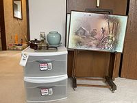 Stack of two Sterilite Clearview plastic storage drawers with ceramic items on top, signed TV trays on wooden stand next to drawers.