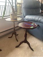 Two wooden pedestal tables side by side next to a blue armchair, one with a potted plant on top.
