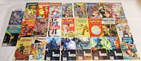 Top view of 26 assorted comic books spread on a surface showing varied colorful covers including cartoons, war, western, and sci-fi themes.