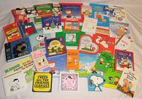 Photo displaying all 36 Peanuts themed books spread out on a surface, showing colorful covers and the variation of hard and soft covers including holiday and activity themed titles.