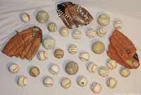 Photo showing three leather baseball gloves (two brown, one orange) and about 27 baseballs and softballs on a white surface, arranged in front of and around the gloves.