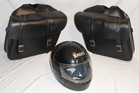 Pair of black leather motorcycle saddlebags with black Raider helmet in front, showing front and side views