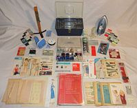 Full overview of sewing and knitting items laid out on fabric, showing sewing box, yarn winder, iron, buttons, patterns and threading supplies.