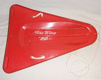 Top view of red triangular steel sled with pull rope tied at front, showing general wear and two white side handles.