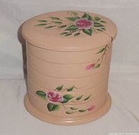 Front view of the closed round jewelry box showing hand-painted pink roses and green leaves on a peach/tan background.