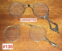 Both antique lorgnettes with oval lenses and decorative handles laid on wooden surface, showing overall condition and size.