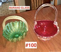 Two vintage Murano glass baskets on wooden table; one green by Seguso, one red attributed to Salviati