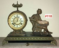 Full front view of cast metal mantel clock with seated figurine on black base; winding key placed in foreground