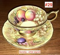 Close-up of teacup and saucer showing hand-painted fruit design and artist signature