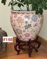 Large Asian stoneware jardiniere on carved wooden stand with detailed floral pattern and pink, blue, yellow, green colors on off-white.