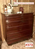 Angled front view showing left side and front of dresser with reflection in glass top and decorative items on top.