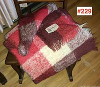 Pair of folded Glen Cree Mohair blankets in red and brown multi-color plaid on a wooden chair showing full blankets and fringed edges